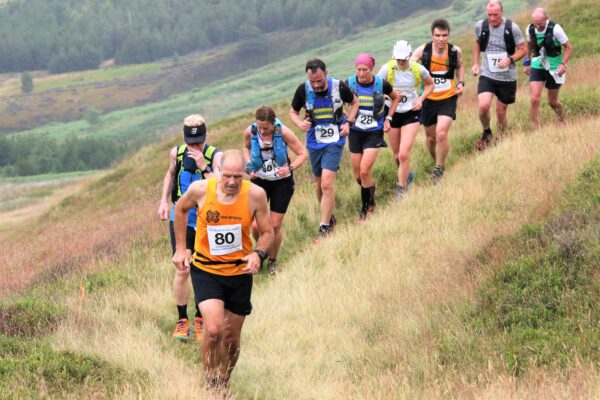 A group of runners in single file on a fairly flat section of moorland